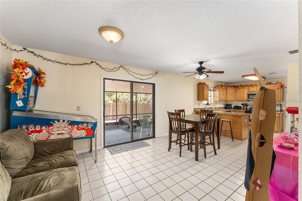 A room with tile flooring, a pinball machine, a dining set, and an open kitchen — 3025 W UNIVERSITY AVENUE, GAINESVILLE, FL