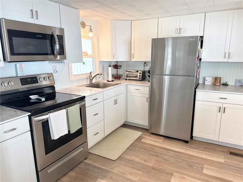 A kitchen features white cabinets, stainless steel appliances, and wood-look flooring — 7214 MOUNT FAIRFIELD ROAD NE UNIT 527, ST PETERSBURG, FL