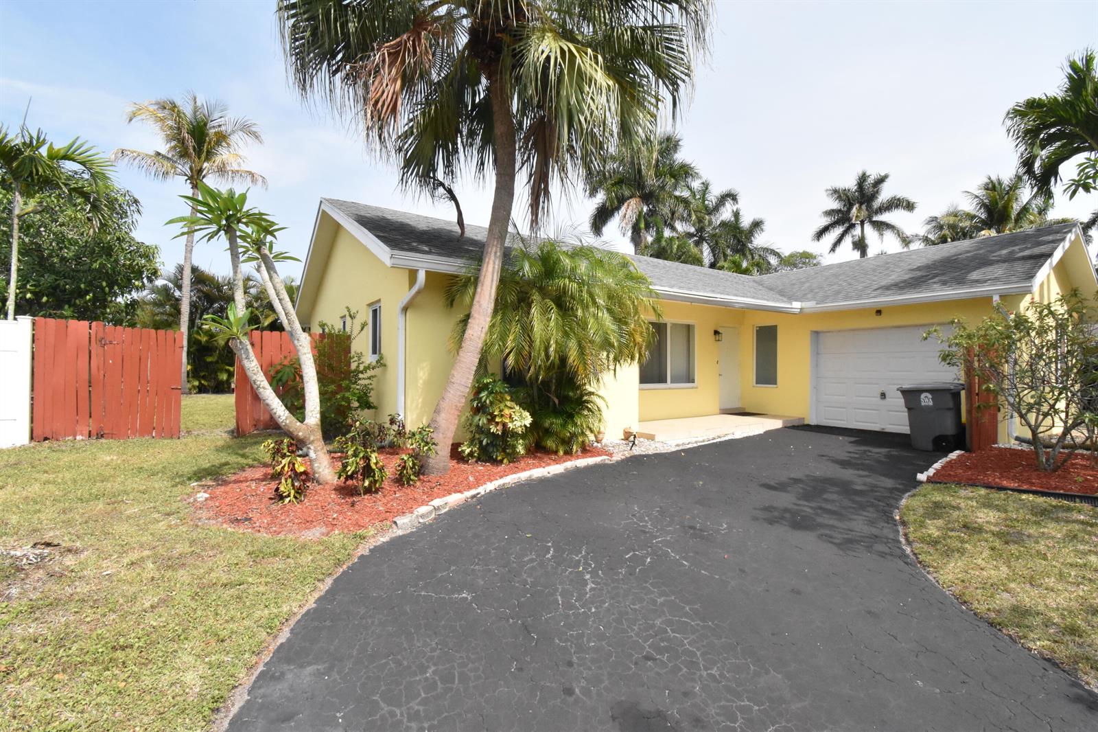 A yellow single-story house features a black asphalt driveway, palm trees, and a red fence — 9426 Southampton Place, Boca Raton FL 33434, BOCA RATON, FL