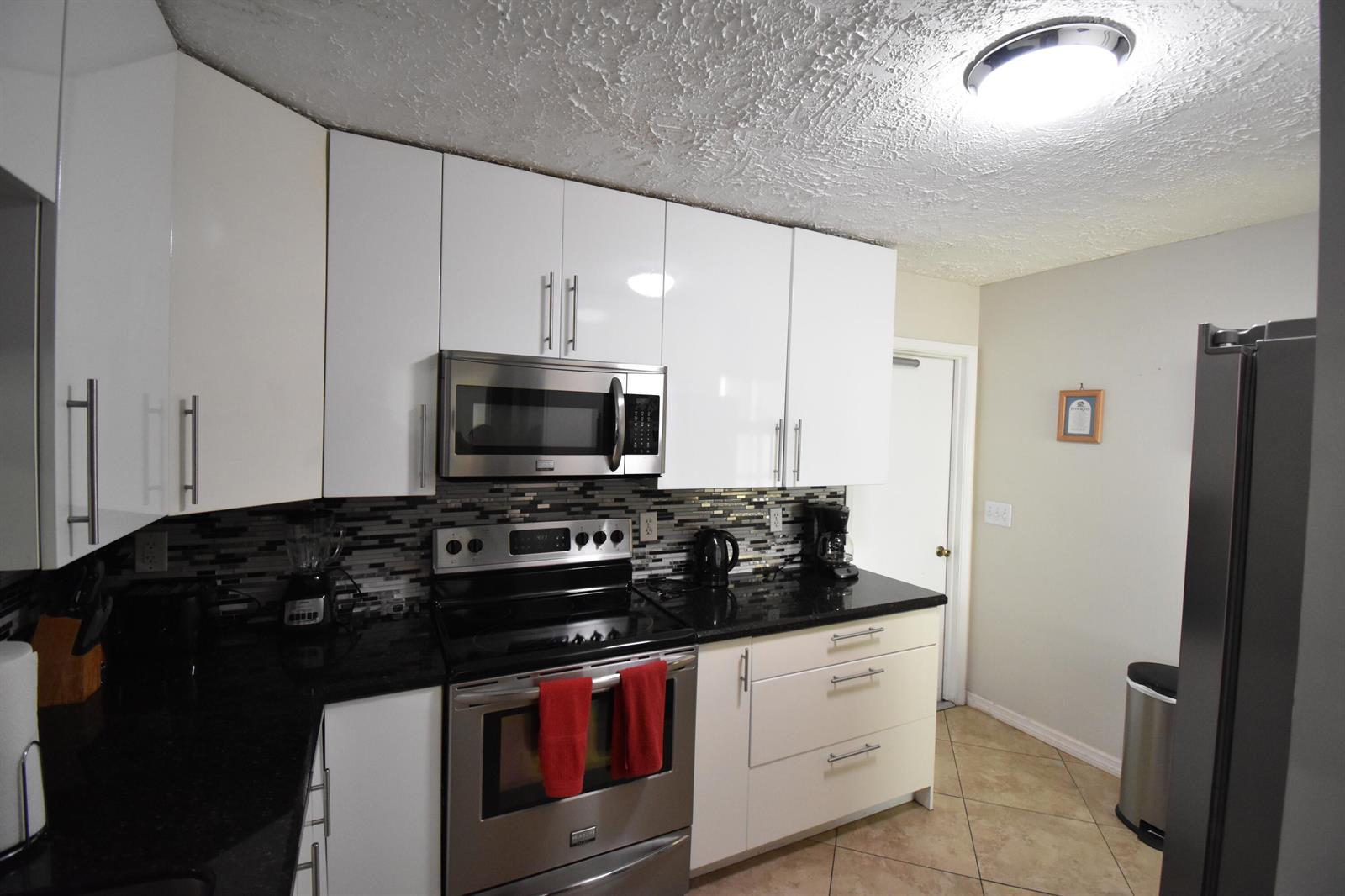 A kitchen features white cabinets, black countertops, stainless steel appliances, and a tiled floor — 9426 Southampton Place, Boca Raton FL 33434, BOCA RATON, FL