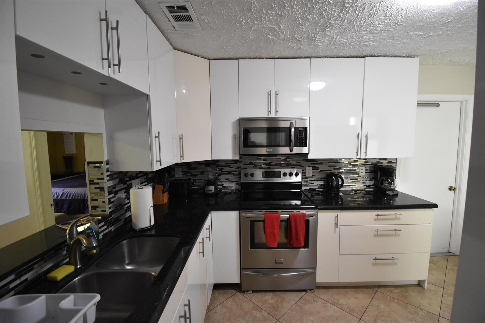 A kitchen features white cabinets, black countertops, stainless steel appliances, and a mosaic tile backsplash — 9426 Southampton Place, Boca Raton FL 33434, BOCA RATON, FL