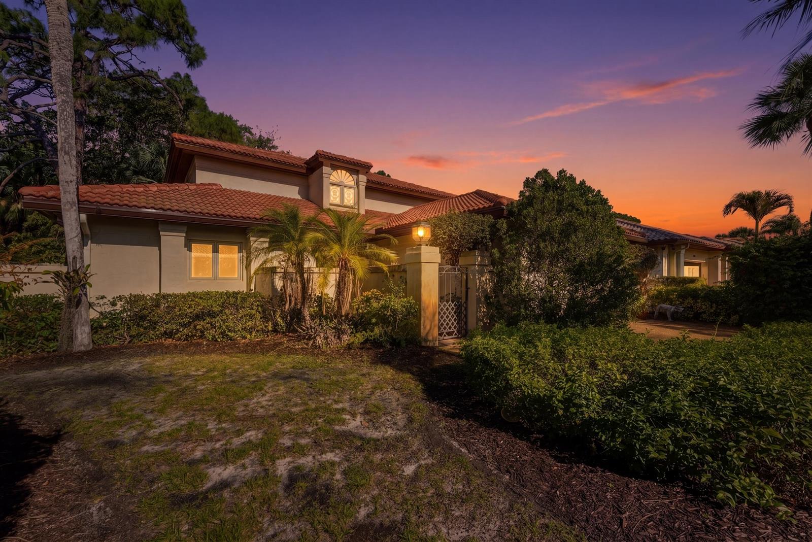 A single-story house with a red tile roof and a gated courtyard at sunset — 5370 SE Merion Way, Stuart FL 34997, STUART, FL