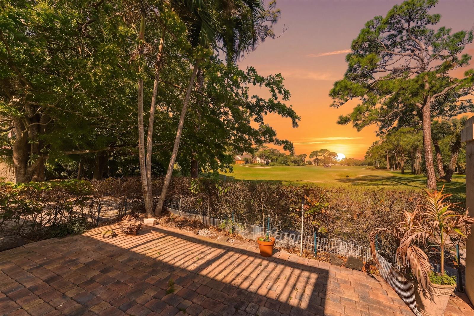 A brick patio overlooks a golf course at sunset with trees and a wire fence — 5370 SE Merion Way, Stuart FL 34997, STUART, FL