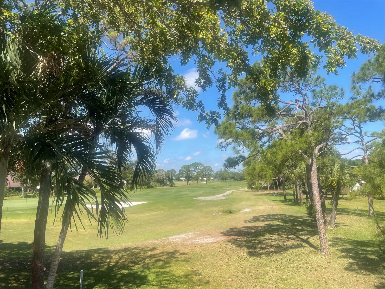 A view of a golf course fairway framed by palm and pine trees under blue skies — 5370 SE Merion Way, Stuart FL 34997, STUART, FL