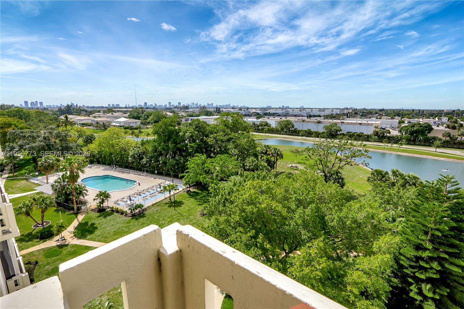 An elevated view from a balcony overlooks a swimming pool, green space, and a lake — 4330 Hillcrest Dr # 807, Hollywood FL 33021, HOLLYWOOD, FL