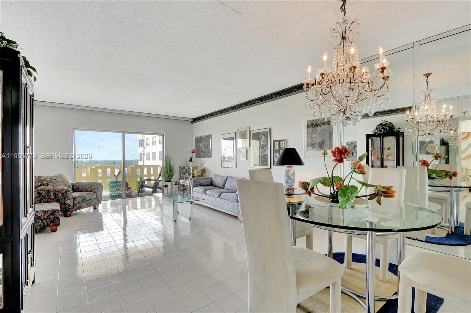 A bright living and dining area features white tile floors, a crystal chandelier, and balcony access — 4330 Hillcrest Dr # 807, Hollywood FL 33021, HOLLYWOOD, FL