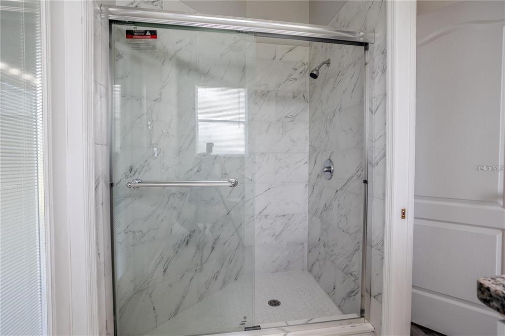 A walk-in shower features white marble-look tile walls, a glass door, and a hexagonal floor — 4946 LAZY OAKS WAY, ST CLOUD, FL
