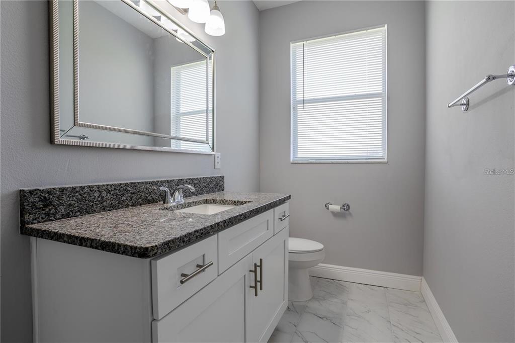 A bathroom features a white vanity with a granite countertop, a mirror, and a toilet — 4946 LAZY OAKS WAY, ST CLOUD, FL
