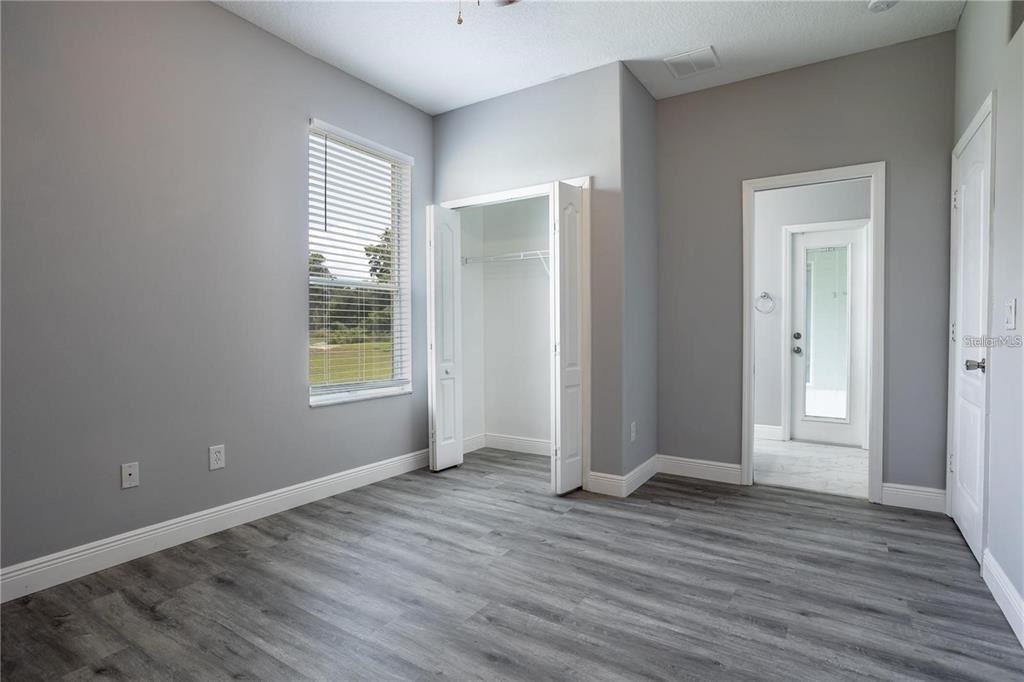 A bedroom with gray walls, wood-look flooring, a window with blinds, a closet, and a doorway — 4946 LAZY OAKS WAY, ST CLOUD, FL