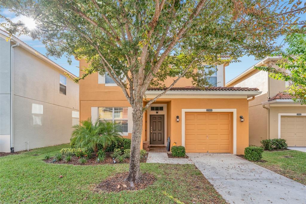 A two-story orange stucco house with a single-car garage and a front yard tree — 2908 BANANA PALM DRIVE, KISSIMMEE, FL