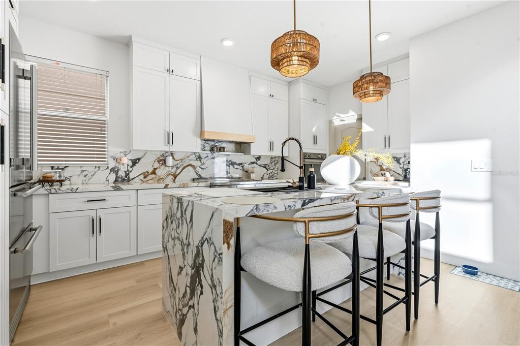 A modern kitchen features white cabinetry, a marble waterfall island, and two woven pendant lights — 2908 BANANA PALM DRIVE, KISSIMMEE, FL
