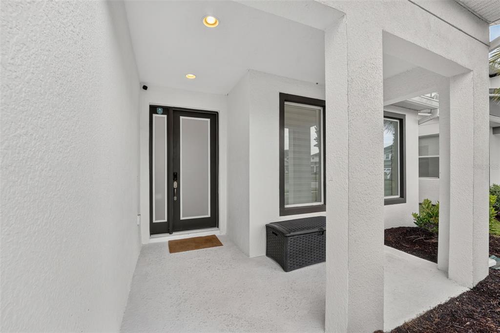 A covered entryway features a dark-framed glass door, a storage chest, and white stucco walls — 2667 CALISTOGA AVENUE, KISSIMMEE, FL