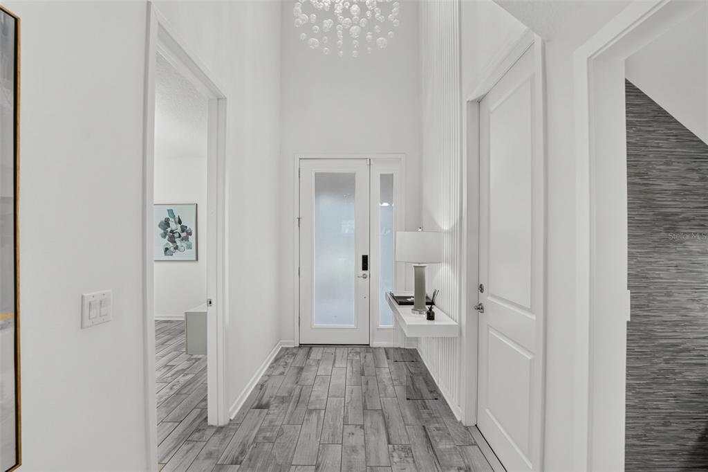 A bright entryway features a glass-paneled front door, wood-look tile flooring, and a modern chandelier — 2667 CALISTOGA AVENUE, KISSIMMEE, FL