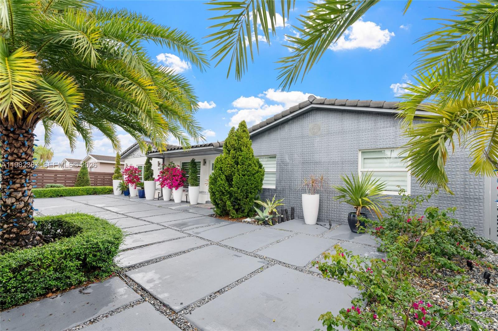 A gray house with a paved driveway, palm trees, and potted plants under a blue sky — 12721 SW 47th St, Miami FL 33175, MIAMI, FL