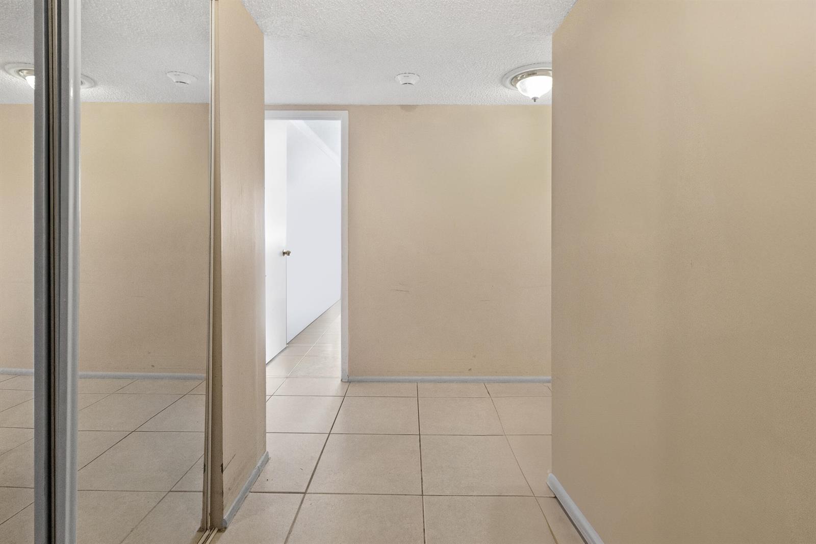 A hallway with beige walls, tiled flooring, a mirrored closet, and a doorway leading ahead — 111 N Pompano Beach Boulevard # 1507, Pompano Beach FL 33062, POMPANO BEACH, FL