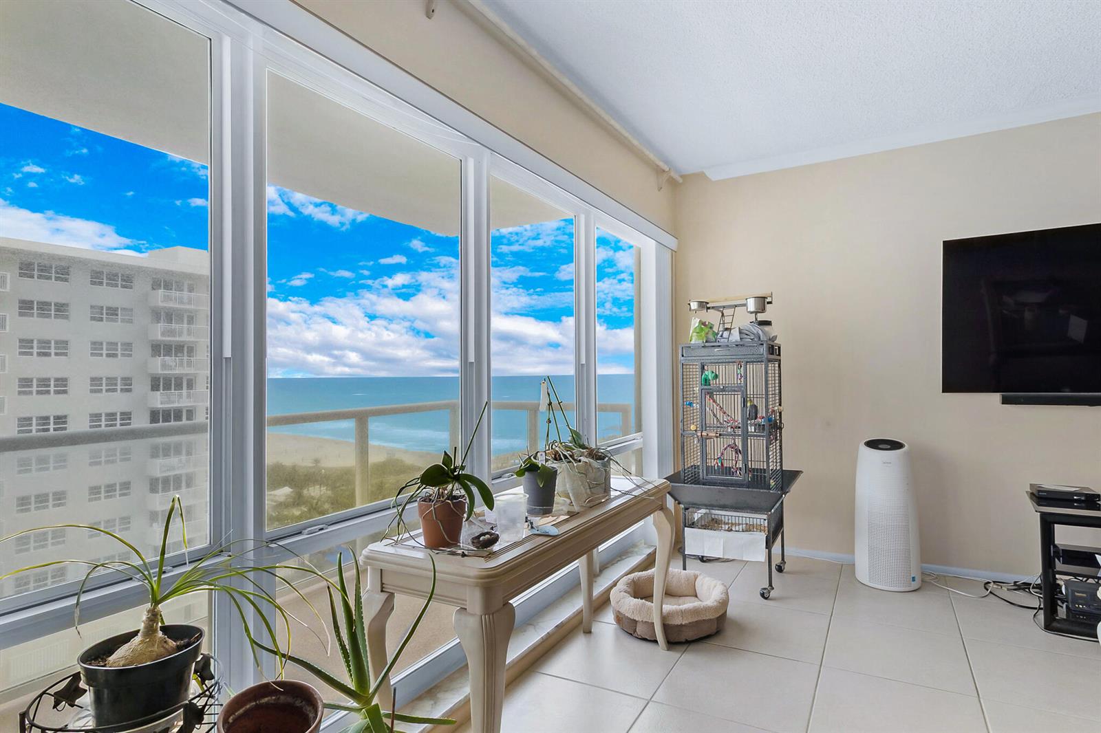 A living area features large windows overlooking the ocean, tiled floors, and a birdcage — 111 N Pompano Beach Boulevard # 1507, Pompano Beach FL 33062, POMPANO BEACH, FL