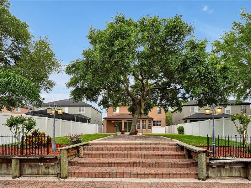 A large tree stands in the center of a brick patio behind a suburban house — 10233 SEROTINA COURT, ORLANDO, FL