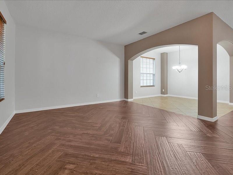 A living room with herringbone wood flooring leads into a dining area with tile — 10233 SEROTINA COURT, ORLANDO, FL
