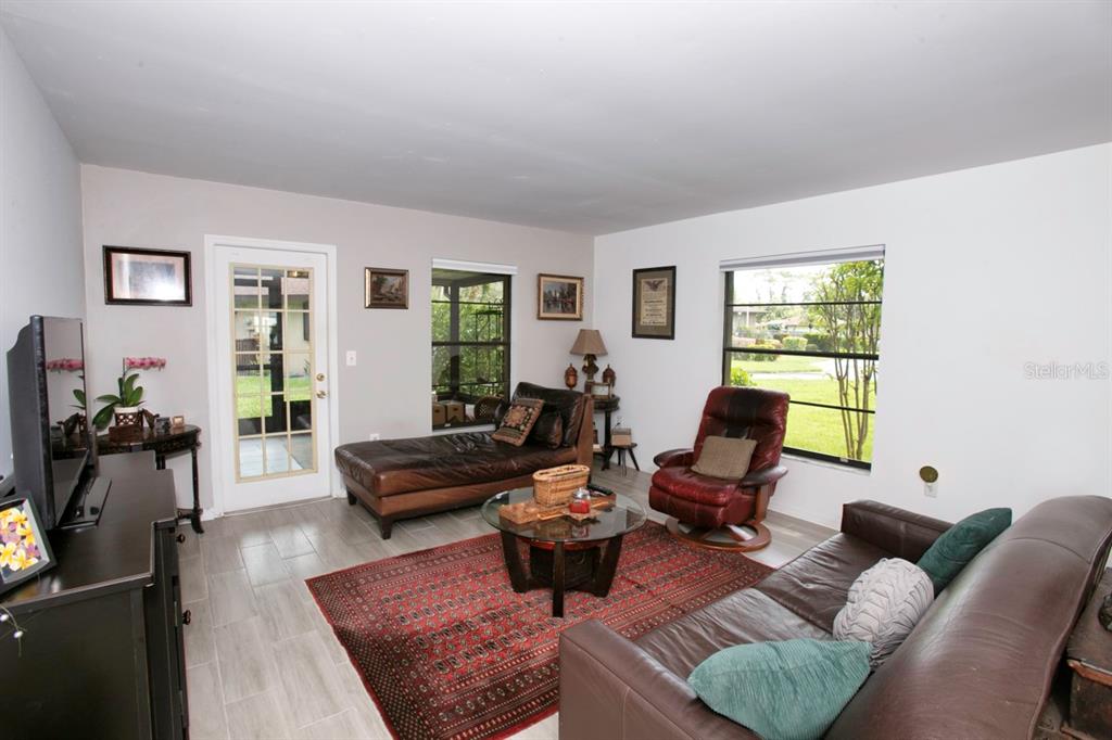 A living room features tile flooring, a red area rug, leather seating, and large windows — 6504 HERITAGE LANE UNIT 99, BRADENTON, FL