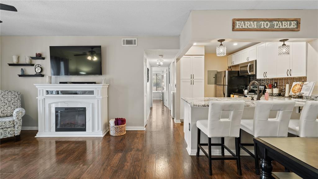 A living room with a fireplace and television connects to a kitchen with white cabinets — 8203 SUN SPRING CIRCLE UNIT 12, ORLANDO, FL