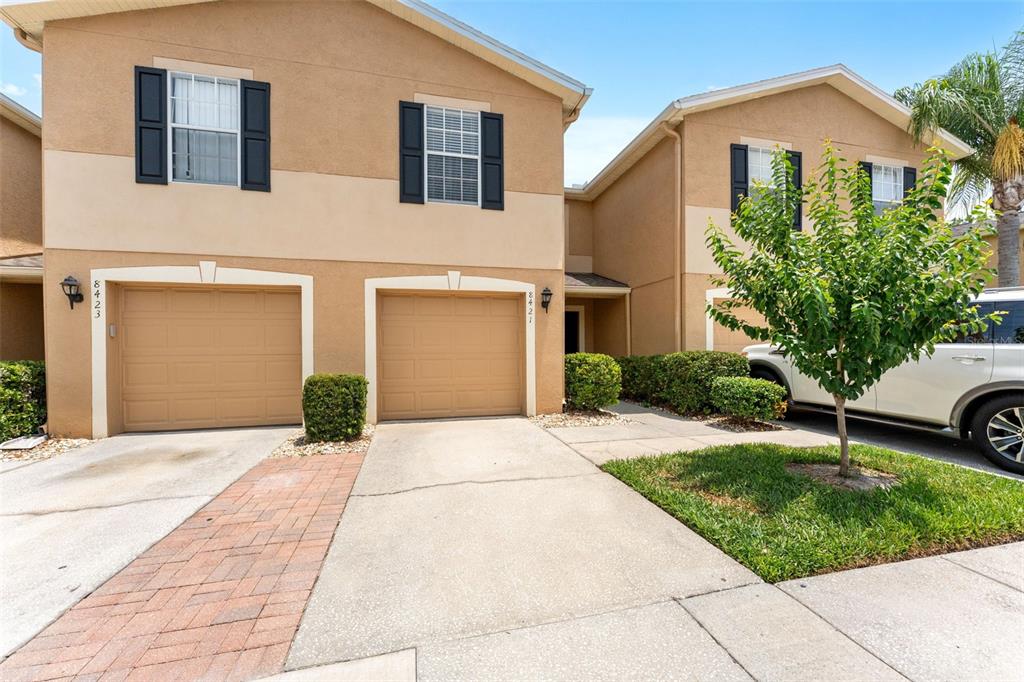 A two-story townhouse exterior features two tan garages, dark shutters, and a paved driveway — 8421 EDGEWATER PLACE BOULEVARD, TAMPA, FL