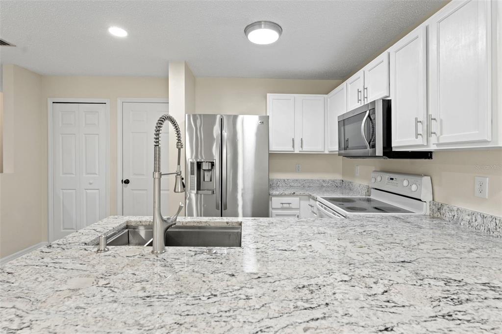 A kitchen with white cabinets, granite countertops, and stainless steel appliances opens to a living area — 8421 EDGEWATER PLACE BOULEVARD, TAMPA, FL