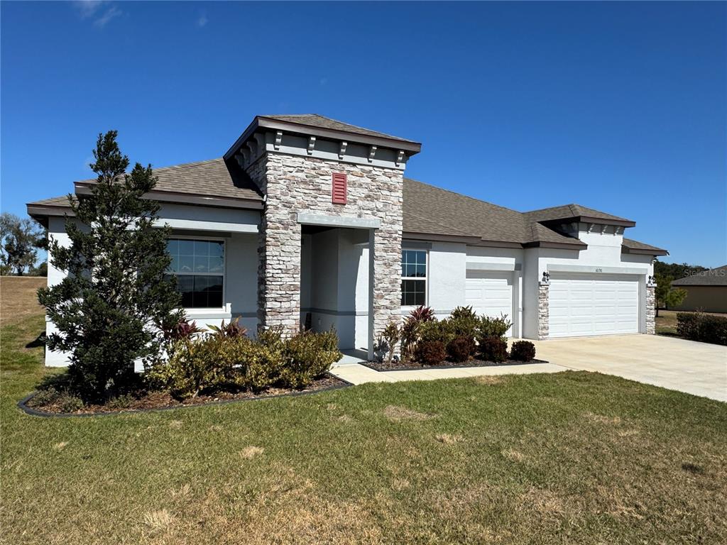 A single-story house with a stone-accented entryway, white stucco walls, and a three-car garage — 10190 DOLPHIN GULL CIRCLE, THONOTOSASSA, FL