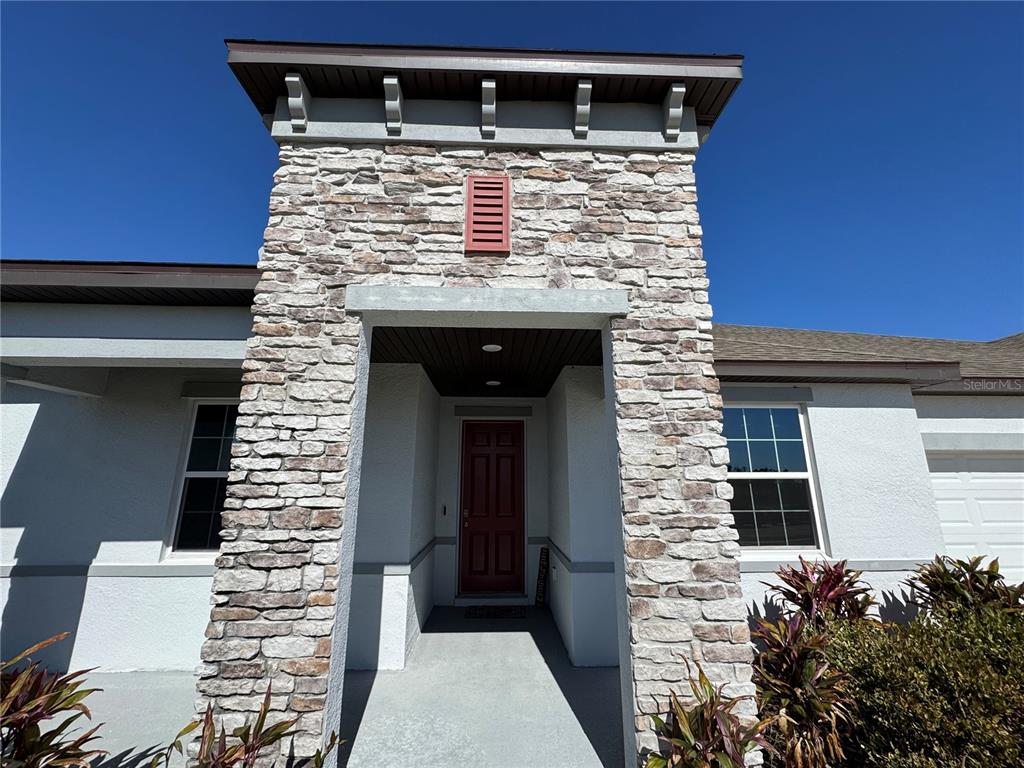 A stone-faced entryway features a red front door and a recessed porch under a roof — 10190 DOLPHIN GULL CIRCLE, THONOTOSASSA, FL