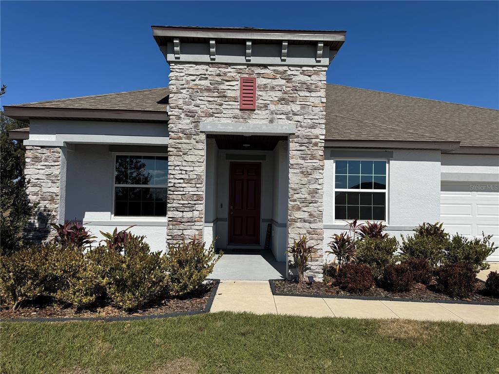 A single-story house exterior features a stone-clad entryway with a red door and landscaping — 10190 DOLPHIN GULL CIRCLE, THONOTOSASSA, FL