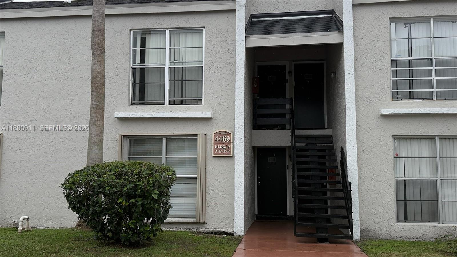 The exterior of a two-story apartment building features a staircase leading to upper-level units — 4469 Treehouse Ln # B, Tamarac FL 33319, TAMARAC, FL