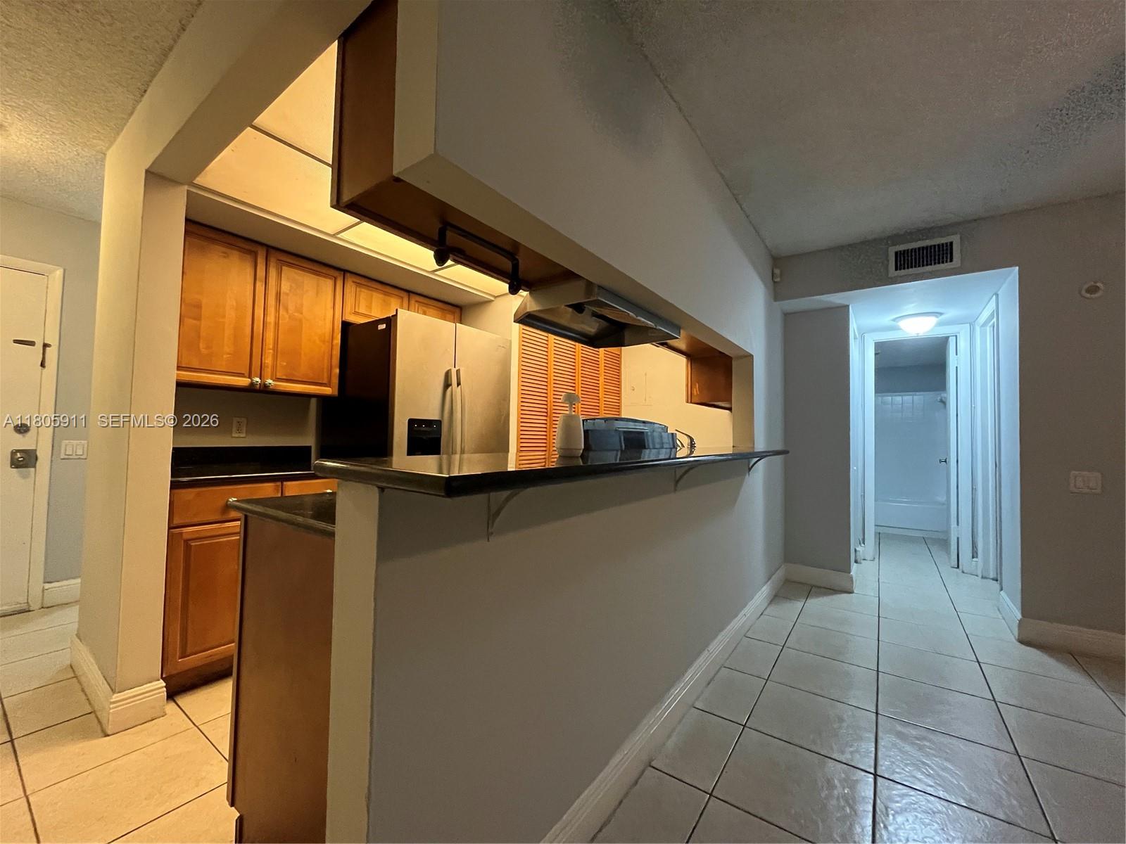 A kitchen with wooden cabinets and a breakfast bar overlooks a tiled hallway — 4469 Treehouse Ln # B, Tamarac FL 33319, TAMARAC, FL