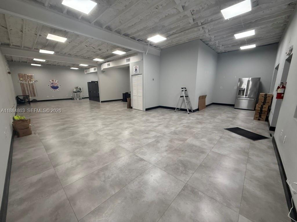 An open commercial space features gray tiled flooring, a white exposed ceiling, and a refrigerator — 7150-7160 NW 5th Pl, Miami FL 33150, MIAMI, FL
