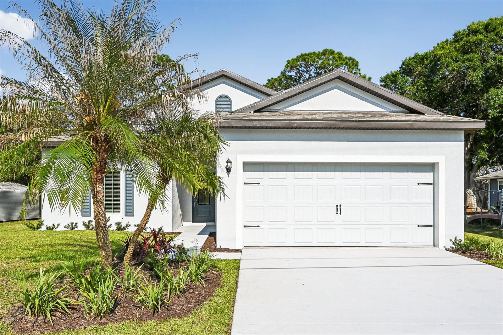 A white single-story house with a two-car garage, a palm tree, and a front walkway — 6010 Hickory Drive, Fort Pierce FL 34982, FORT PIERCE, FL