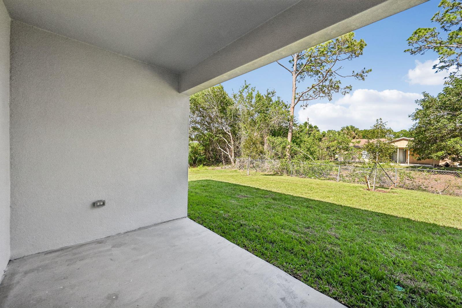 A concrete patio overlooks a grassy backyard enclosed by a chain-link fence — 6010 Hickory Drive, Fort Pierce FL 34982, FORT PIERCE, FL