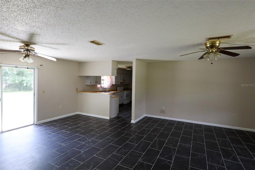 A spacious room with dark tile flooring, two ceiling fans, and an open kitchen area — 66 SILVER LANE, OCALA, FL