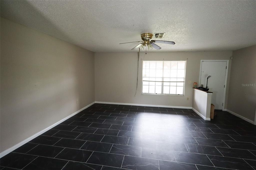 An empty room features dark rectangular floor tiles, beige walls, and a ceiling fan — 66 SILVER LANE, OCALA, FL