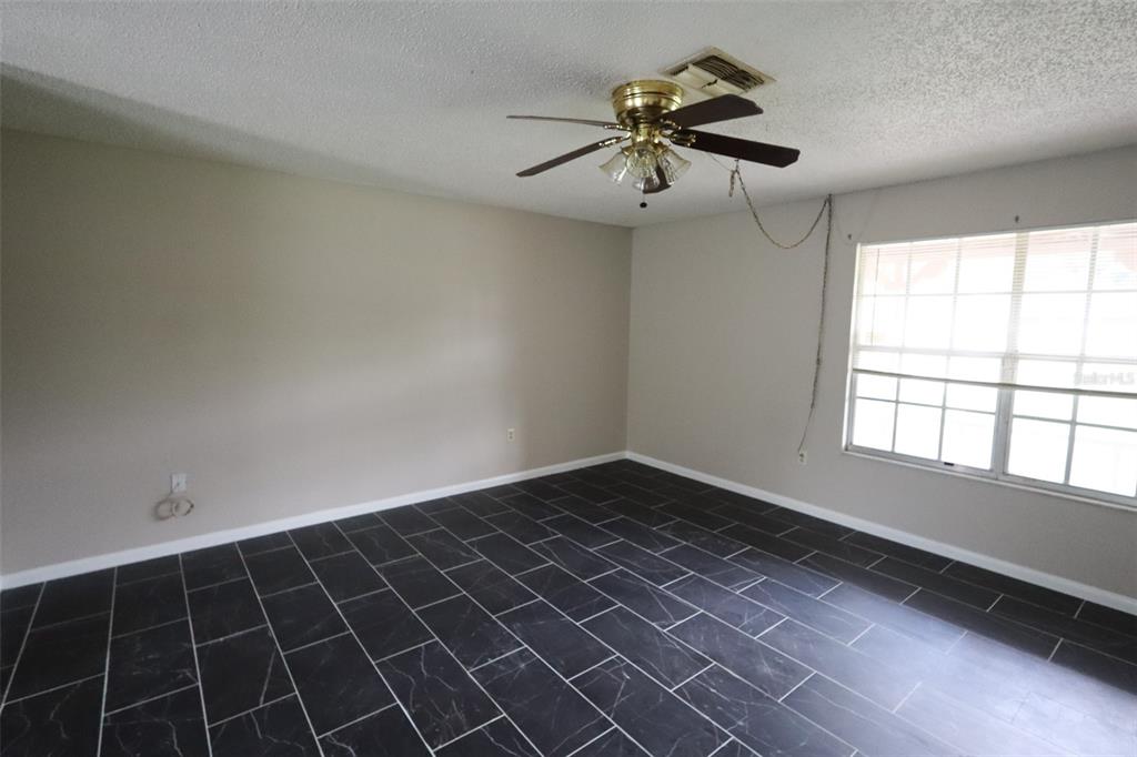 An empty room features dark marble-look tile flooring, light-colored walls, and a ceiling fan — 66 SILVER LANE, OCALA, FL