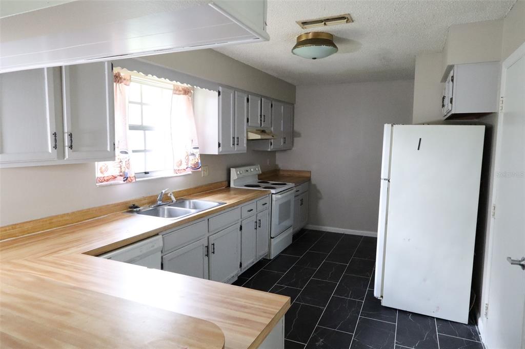 A kitchen features light gray cabinets, wood-look laminate countertops, white appliances, and dark tile flooring — 66 SILVER LANE, OCALA, FL