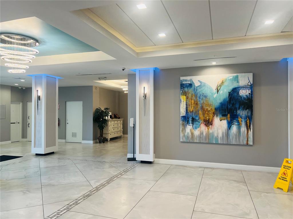 A modern lobby features white tile floors, recessed lighting, a crystal chandelier, and abstract wall art — 1909 SOUTH ATLANTIC AVENUE UNIT 405/406, DAYTONA BEACH SHORES, FL
