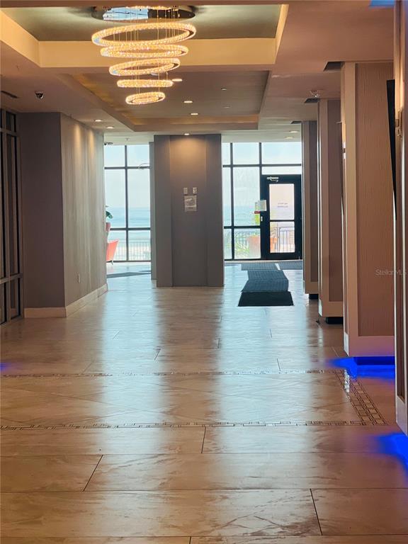 A modern lobby features tiled floors, a tiered circular chandelier, and floor-to-ceiling windows overlooking water — 1909 SOUTH ATLANTIC AVENUE UNIT 405/406, DAYTONA BEACH SHORES, FL