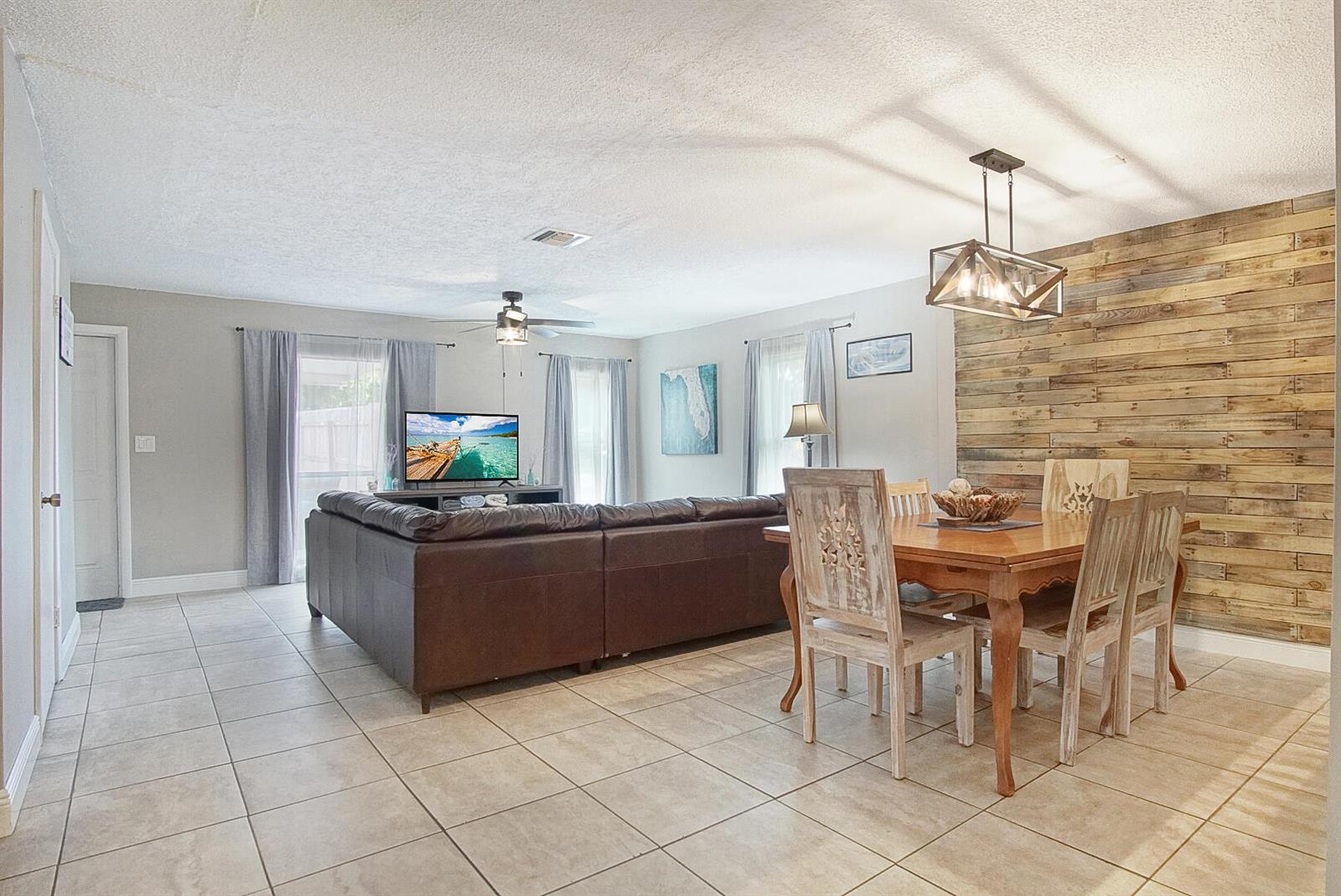 A living and dining area features tile flooring, a wood-plank accent wall, and a sectional sofa — 1002 Avenue E, Fort Pierce FL 34950, FORT PIERCE, FL
