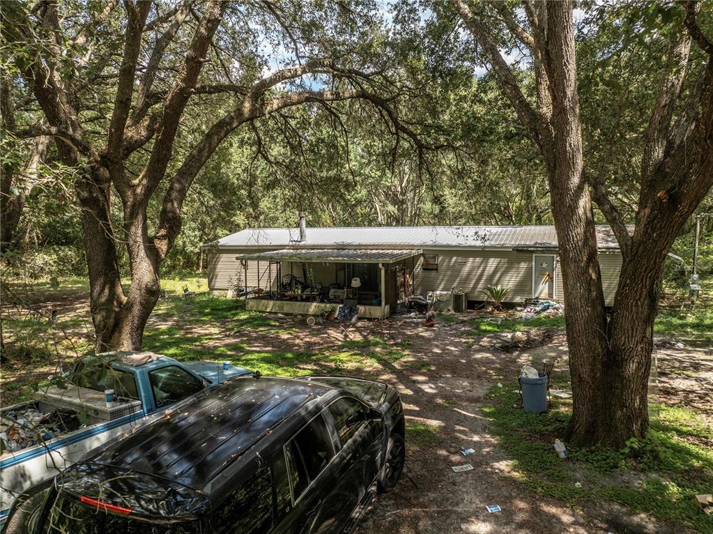 A single-story house with a metal roof sits in a wooded lot with two vehicles — 2946 SE 21ST AVENUE, SUMTERVILLE, FL