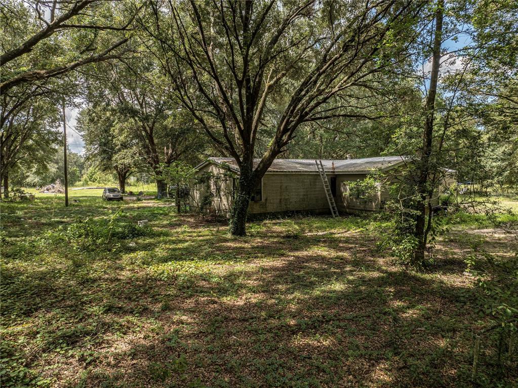 A single-story house with a metal roof sits in a wooded lot with a ladder — 2946 SE 21ST AVENUE, SUMTERVILLE, FL