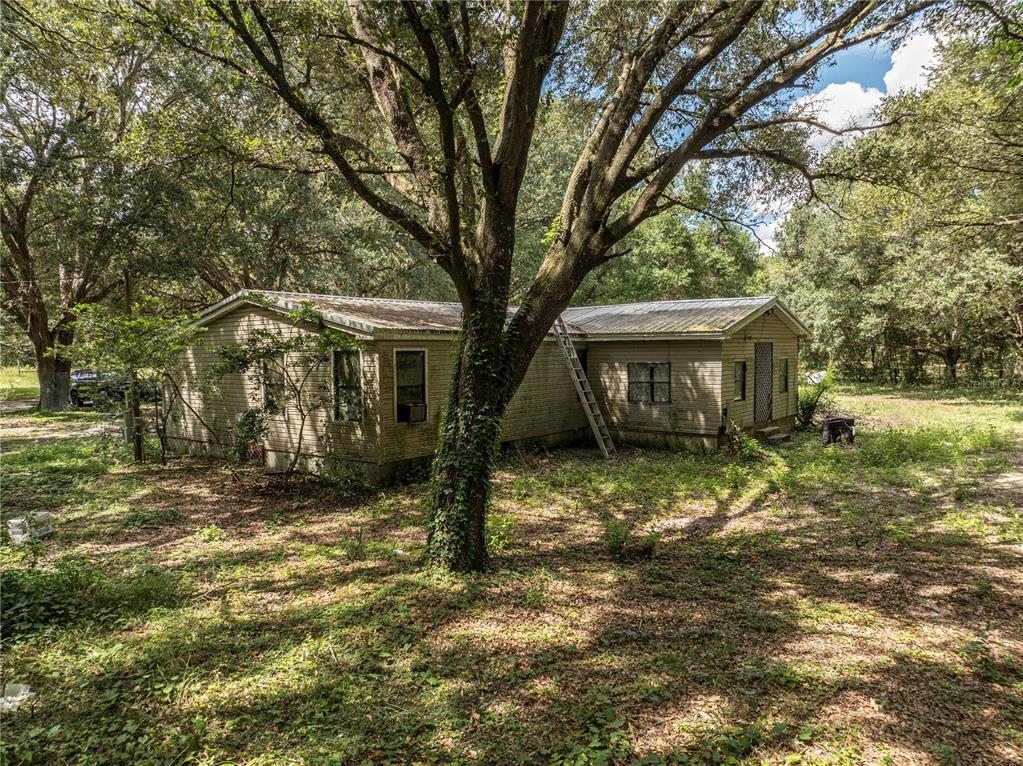 A single-story mobile home with light siding sits in a wooded lot under large trees — 2946 SE 21ST AVENUE, SUMTERVILLE, FL