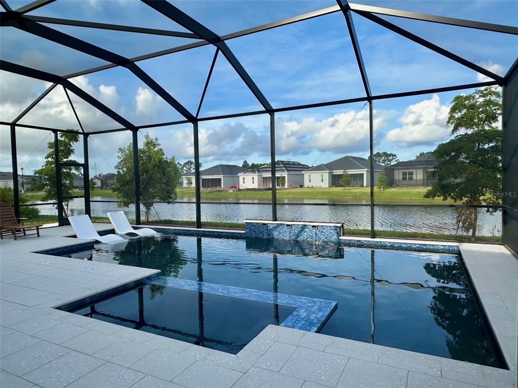 A screened-in swimming pool with a tiled water feature overlooks a lake and neighboring houses — 17577 SANTORINI COURT, VENICE, FL