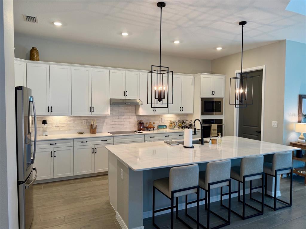 A modern kitchen features white cabinetry, a large marble-topped island, and two black pendant lights — 17577 SANTORINI COURT, VENICE, FL