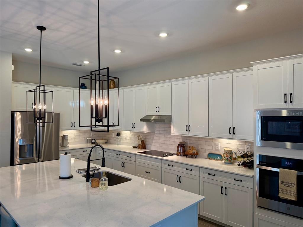 A modern kitchen features white cabinets, stainless steel appliances, a large island, and pendant lighting — 17577 SANTORINI COURT, VENICE, FL