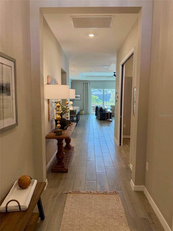 A long hallway with wood-look tile flooring leads to an open living area with large windows — 17577 SANTORINI COURT, VENICE, FL