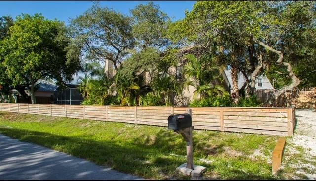 A wooden fence surrounds a house partially obscured by trees and a mailbox in front — 5311 CREEK DRIVE, SARASOTA, FL