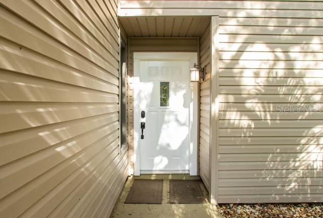 A white front door with a small window is set within a tan vinyl-sided entryway — 5311 CREEK DRIVE, SARASOTA, FL